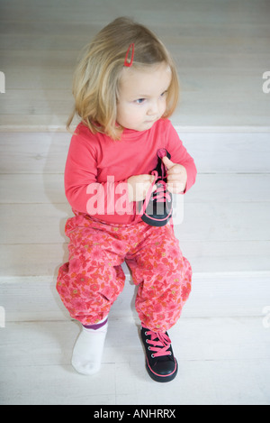 Blonde girl sitting on steps, portant une chaussure, en maintenant les autres en part Banque D'Images