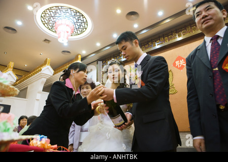 Aider la femme mariée et le marié ouvrir la bouteille de champagne, low angle view Banque D'Images