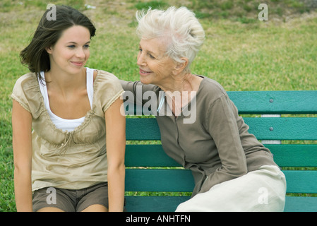 Grand-mère et petite-fille d'adolescent assis ensemble sur un banc, les deux smiling Banque D'Images