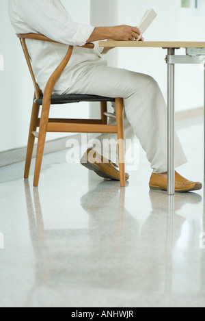 Young man sitting at table reading book, la poitrine vers le bas, side view Banque D'Images