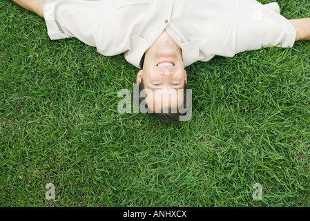 Homme couché à l'envers dans l'herbe, smiling at camera, portrait high angle view Banque D'Images
