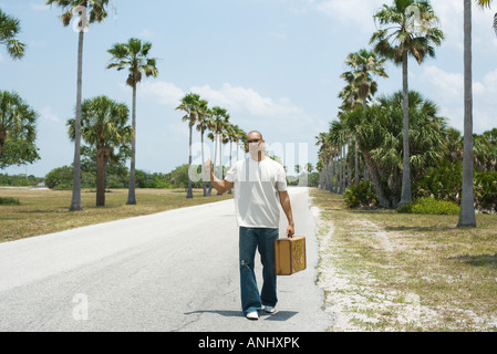 L'homme à côté de l'auto-stop road, transportant suitcase Banque D'Images