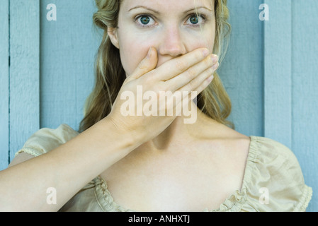 Femme couvrant la bouche avec la main, regardant avec de grands yeux l'appareil photo Banque D'Images