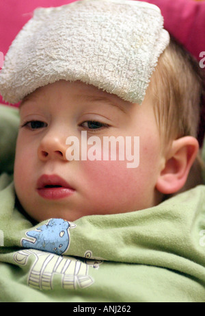 Close up portrait vertical d'un enfant malade avec de la fièvre, avec un tissu froid sur le front. Banque D'Images
