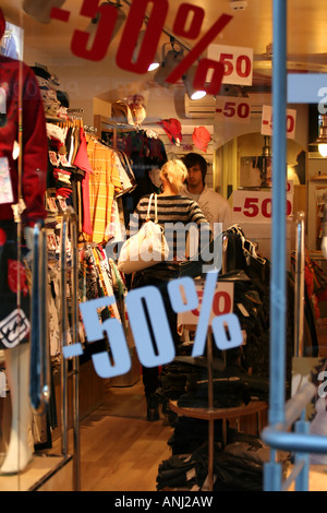 Fenêtre de la boutique de vêtements avec autocollants de solde à -50%. Personnes méconnaissables vues à l'intérieur du magasin. Banque D'Images