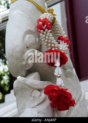 Sculpture et de guirlande de fleurs rouges dans un temple bouddhiste à Bangkok, Thaïlande. Banque D'Images