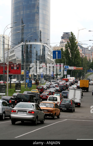 Embouteillages dans une rue animée de Kiev avec des voitures, des bus et des camions sous un bâtiment en verre moderne et des grues de construction en arrière-plan. Banque D'Images