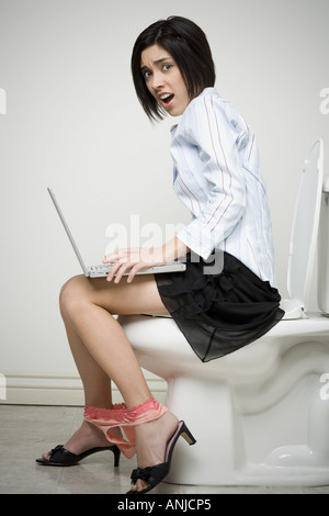 Portrait d'une femme assis sur une toilette avec un ordinateur portable Banque D'Images