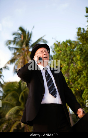 Maldives bourreau de businessman en chapeau melon et costume talking on mobile phone marcher le long de la plage tropicale Banque D'Images