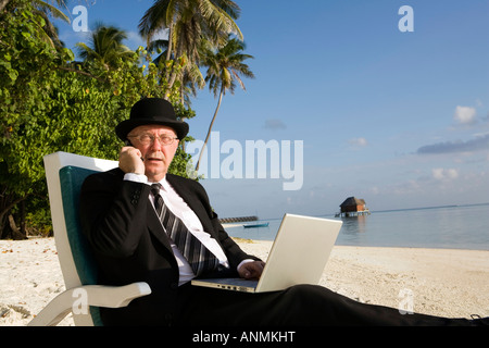 Homme d'affaires en chapeau melon et costume d'affaires travaillant sur un ordinateur portable tout en talking on mobile phone on tropical beach Banque D'Images