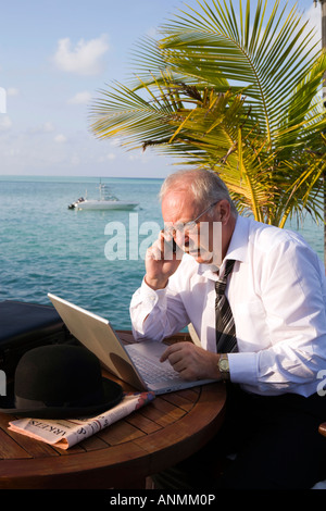 Chemise homme en travaillant sur un ordinateur portable talking on mobile phone in lieu tropical Banque D'Images