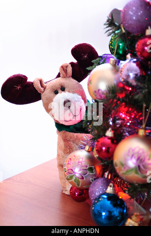Un renne à motif jouet s'infiltre derrière l'arbre de Noël décoré de boules Banque D'Images