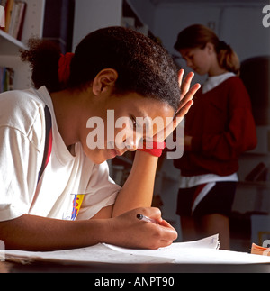 Les études d'écolière junior Afro Antillais attentivement dans la bibliothèque de l'école Banque D'Images
