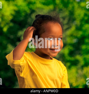 Bébé mignon joli Afro Antillais 4ans fille noire pose pour l'appareil photo en situation ensoleillée jardin portant des T-shirt jaune vif Banque D'Images