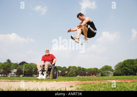 Long man jumping avec un homme d'âge moyen dans un fauteuil roulant et de le regarder Banque D'Images