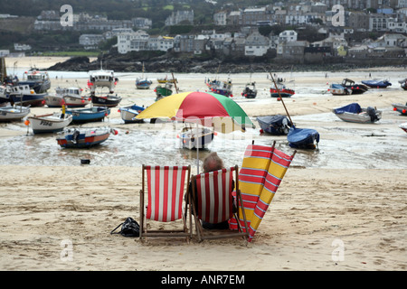 Un homme assis dans une chaise longue sur le sable de St Ives Harbour à marée basse l'Angleterre Cornwall Banque D'Images