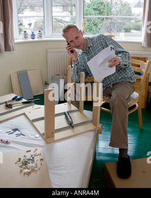 L'homme à la difficulté à construire des meubles paquet plat appelant à l'aide d'un ami ou d'un service d'assistance téléphonique Banque D'Images