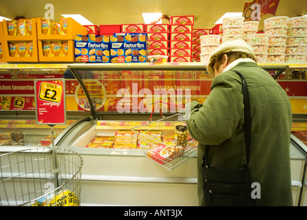 Seule femme mature avec fil panier à la recherche dans un congélateur d'aliments surgelés, de l'Islande Supermarché, Aberystwyth, Pays de Galles, Royaume-Uni Banque D'Images