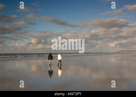 Deux personnes marchant le long de la plage de sable à l'ouest du pays de Galles Borth le jour de Noël 2007 avec leurs reflets dans le sable humide, UK Banque D'Images