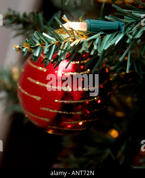 Une boule de Noël rouge brillant se bloque à partir d'un arbre de Noël artificiel. Banque D'Images