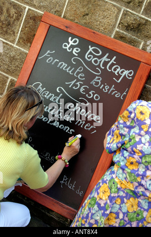 Woman writing on blackboard menu restaurant extérieur à Dinan Bretagne France Banque D'Images