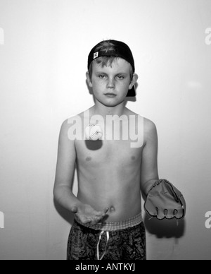 Un B&W Image d'un garçon de 13 ans portant un chapeau de base-ball & Mitt,faire du rattrapage avec une balle de baseball dans sa chambre. Banque D'Images