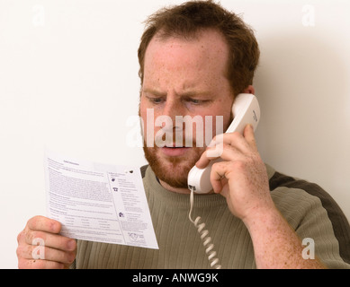 L'homme sur le téléphone en question des éléments sur ses relevés bancaires montrant surpris surprise ou d'horreur Banque D'Images