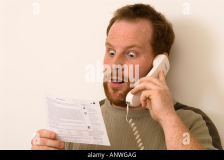 L'homme sur le téléphone en question des éléments sur ses relevés bancaires montrant surpris surprise ou d'horreur Banque D'Images