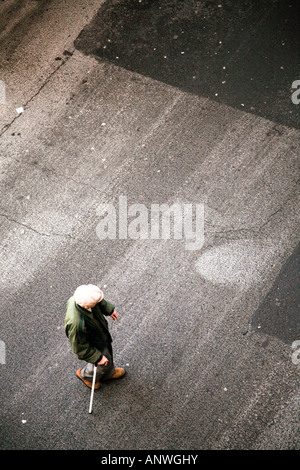 Vieux homme plafonné avec bâton de marche crossing road prises d'en haut Banque D'Images