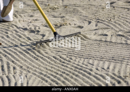 Golfeuse aplatit le sable d'un bunker avec un râteau Banque D'Images