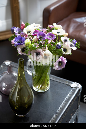 Fleurs colorées dans une cruche en verre sur un coffre dans la salle de séjour avec un fauteuil en cuir à l'arrière-plan et cadre d'or Banque D'Images