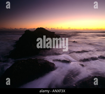 Coucher de soleil sur la mer et les rochers avec de l'eau tourbillonnant autour de la base des rochers et de mousse donnant une impression surréaliste ethereal Banque D'Images