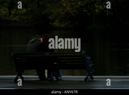 Couple cuddling on park bench par lake dans Autmn light Banque D'Images