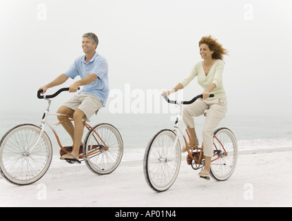 Mature couple riding bikes on beach Banque D'Images