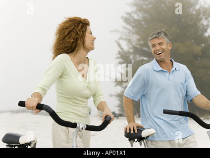 Mature couple walking avec des vélos sur la plage Banque D'Images