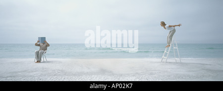 On beach, man holding up livre en face de visage tout en femme sur l'escabeau lui crie Banque D'Images