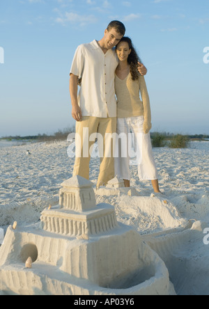 Couple standing on beach looking at château de sable Banque D'Images