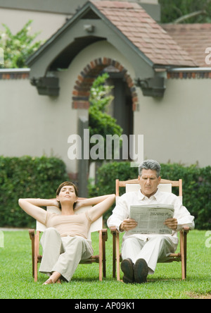 Couple assis dans des chaises longues sur la pelouse, Man reading newspaper and woman napping Banque D'Images