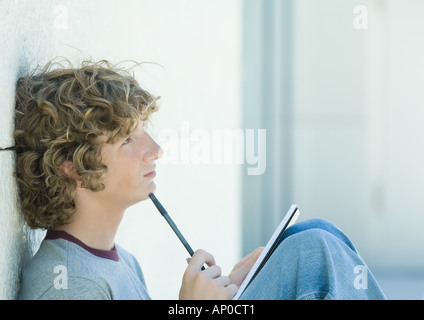 Teenage boy avec stylo et bloc-notes, side view Banque D'Images