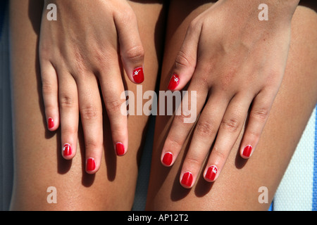 Close-up of an asian teenage girls' les mains sur ses jambes avec des ongles peints en rouge Banque D'Images