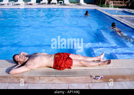 L'homme se reposant sur le côté de la piscine avec woman in background Banque D'Images