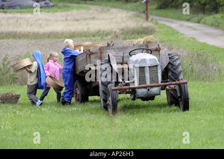 Les cultures de chargement des écoliers dans une remorque à l'arrière d'un tracteur dans le cadre d'une sortie scolaire à la ferme Banque D'Images