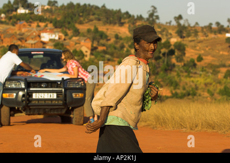 Deux personnes regardant une carte sur le capot d'une voiture à l'arrière-plan, une femme de la région de traverser la route en avant-plan, Madagasca Banque D'Images