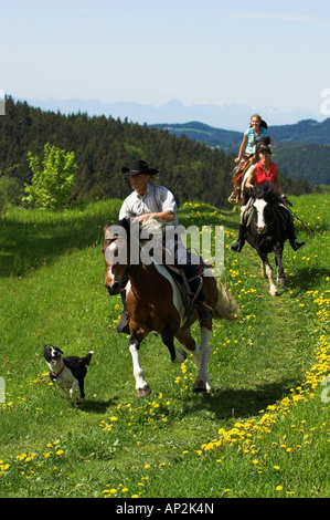 Trois cavaliers trottant à travers une prairie avec un chien, Muehlviertel, Haute Autriche, Autriche Banque D'Images