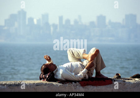 Homme indien couché sur le mur sur Marine Drive avec des gratte-ciel en arrière-plan, Mumbai, Inde du Sud Banque D'Images