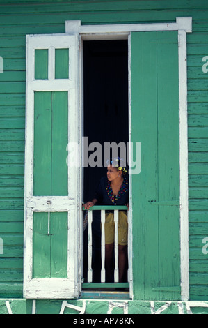 Femme debout dans la fenêtre d'une maison en bois coloré, Barahona, République Dominicaine Banque D'Images
