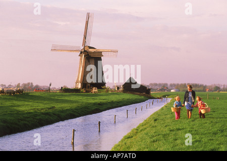 La mère et les enfants avec des paniers traversant les terres agricoles en Hollande près de Windmill et canal Banque D'Images