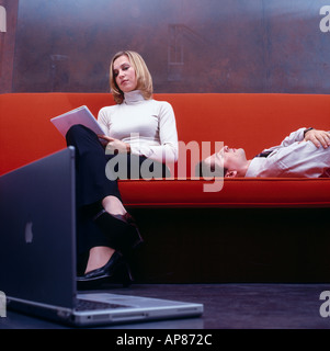 Businesswoman reading documents avec businessman sleeping on a couch Banque D'Images