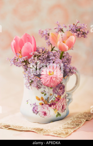 Lilas et tulipes dans un mug floral sur une table avec l'arrière-plan de couleur pastel. Banque D'Images