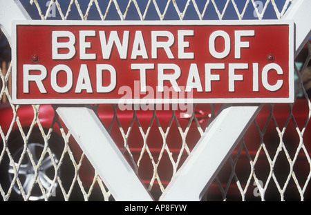 Bold metal sign peint en blanc sur rouge écarlate sur gate avec voiture rouge passé et méfiez-vous du trafic routier indiquant Banque D'Images